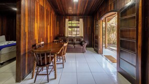 A wooden interior with a dining table and chairs, a sofa, and a window with curtains. - Hotel Fazenda da APM by Bhomy (Caieiras)