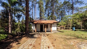 A small house with a tiled roof, surrounded by tall trees and a stone pathway leading to the entrance. - Hotel Fazenda da APM by Bhomy (Caieiras)