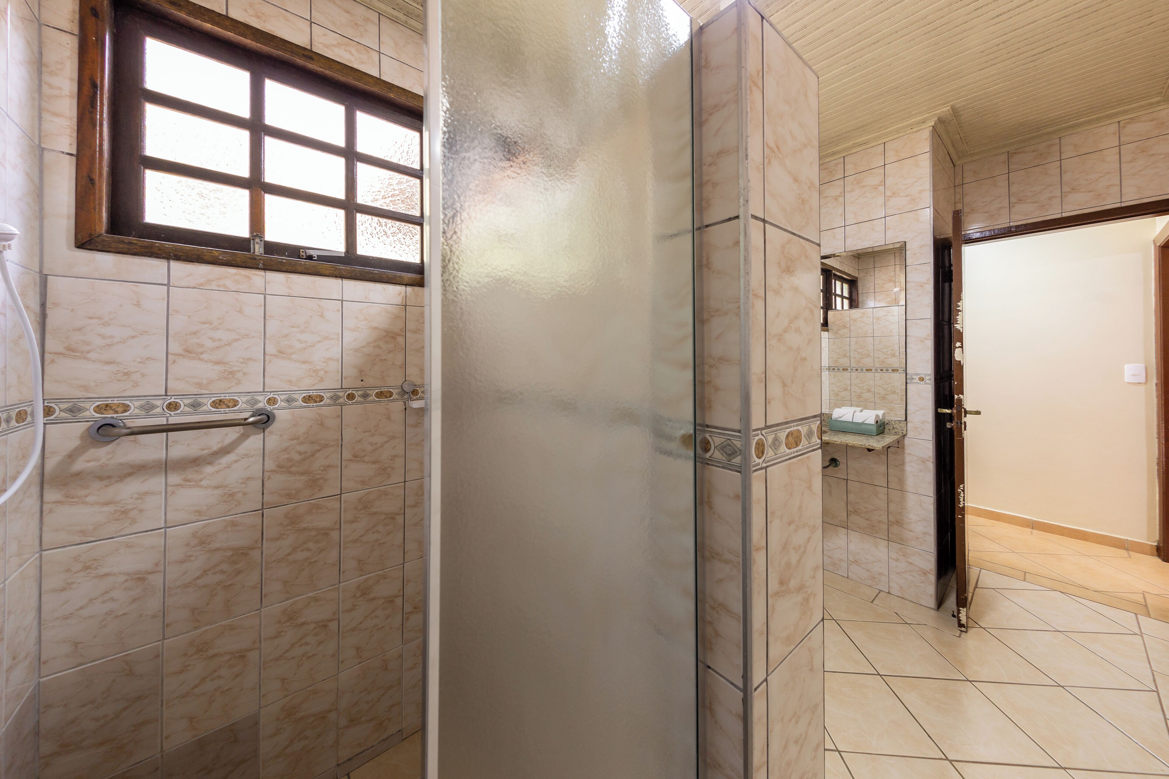 Casa de banho com barra de apoio, espelho e chão em azulejos.