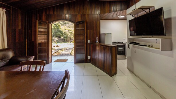 A spacious room with a wooden ceiling and walls, a dining area with a table and chairs, a kitchen area with a refrigerator and stove, and a large TV mounted on the wall. - Hotel Fazenda da APM by Bhomy (Caieiras)