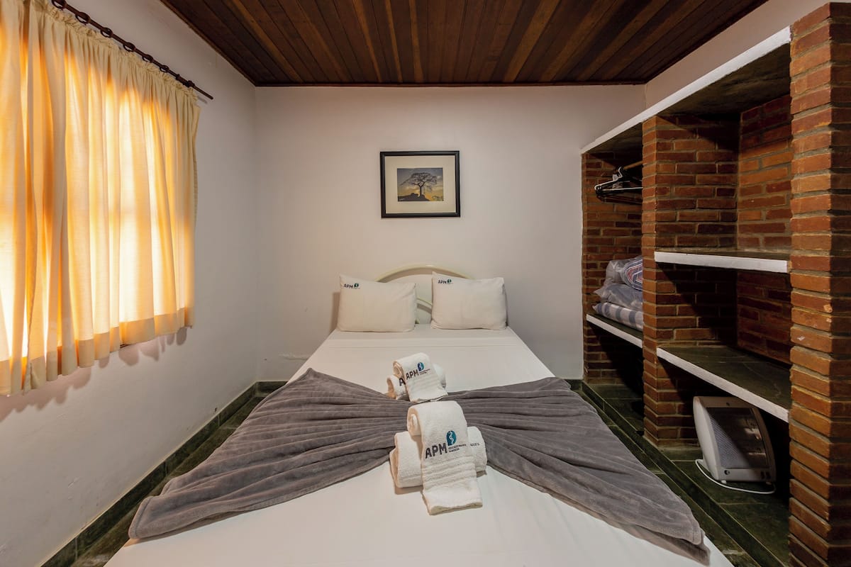 A hotel room with a bed, pillows, a framed picture on the wall, and a brick fireplace.
