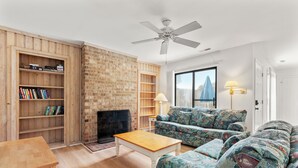 A living room with a brick wall, wooden shelves, a sofa, a coffee table, and a ceiling fan.