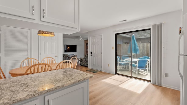 A modern kitchen with white cabinets, a granite countertop, and a dining area with wooden chairs.
