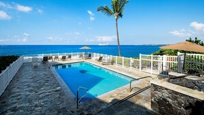 A pool area with a view of the ocean, a palm tree, and a white fence. - Cozy Ocean View 1-bedroom, 1 bath condo in awesome Kailua-Kona with AC (Kailua-Kona)