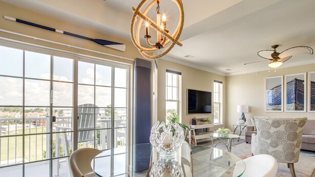 A spacious living room with a glass table, white chairs, a TV, and a balcony with a view. - Welcome to a Cozy Waterfront Condo in Charming Cambridge, MD (Cambridge)