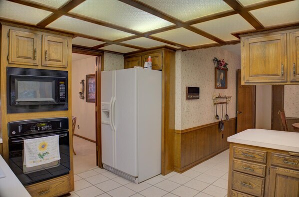Eine Küche mit Holzschränken, einer Mikrowelle, einem Backofen, einem Kühlschrank und einem gefliesten Boden.