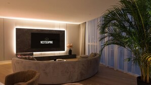 Ein modernes Wohnzimmer mit einem großen Flachbildfernseher, einer gebogenen Couch und einer Topfpflanze.
