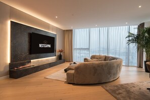 Un salon moderne doté d’un téléviseur à écran plat, d’une cheminée, d’une grande fenêtre et d’un canapé confortable.