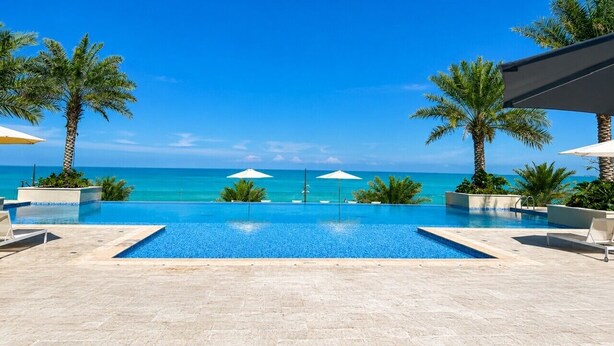 Ein klarer, blauer Himmel, ein Swimmingpool mit Meerblick und Palmen.