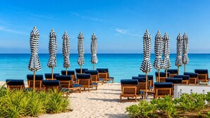 Ein Hotel am Strand mit Reihen von gestreiften Sonnenschirmen und Liegestühlen, die zum Meer ausgerichtet sind.