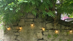 A stone wall with ivy and string lights, two white metal chairs, and a small round table. - Riverside Cottage (Newton Aycliffe)