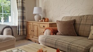 A cozy living room with a sofa, a wooden cabinet, and a decorative table centerpiece. - Riverside Cottage (Newton Aycliffe)