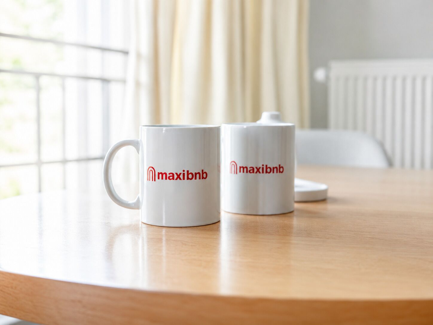 Two white mugs with 'maxibnb' logo on a round wooden table.