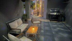 A modern outdoor living area with a sofa, chairs, a table, and a grill.