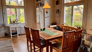 A cozy dining area with a wooden table and chairs, a small kitchen area with a refrigerator, and large windows offering a view of the outdoors. - 4 Star Holiday Home in Nykoping (Ålberga)