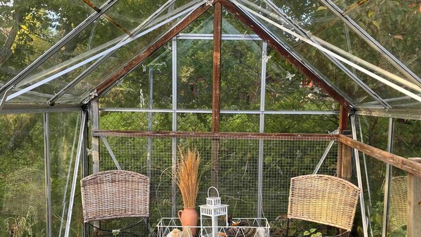 A greenhouse with a glass roof, two wicker chairs, a small table, and a white birdcage. - 4 Star Holiday Home in Nykoping (Ålberga)