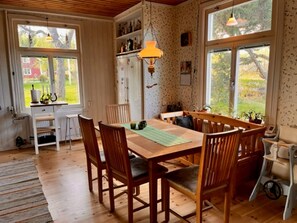 Ein Essbereich mit einem Holztisch und Stühlen, einem Fenster mit Blick ins Grüne und einem Regal mit Flaschen.