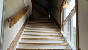 A wooden staircase with white risers and a wooden handrail, leading to a room with a window. - 4 Star Holiday Home in Nykoping (Ålberga)