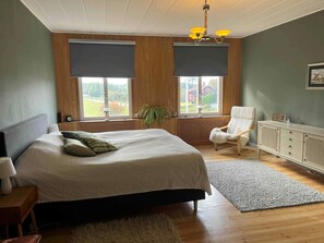 Ein Schlafzimmer mit einem Bett, einem Sessel, einer Heizung und einem Fenster mit Blick auf ein Haus.