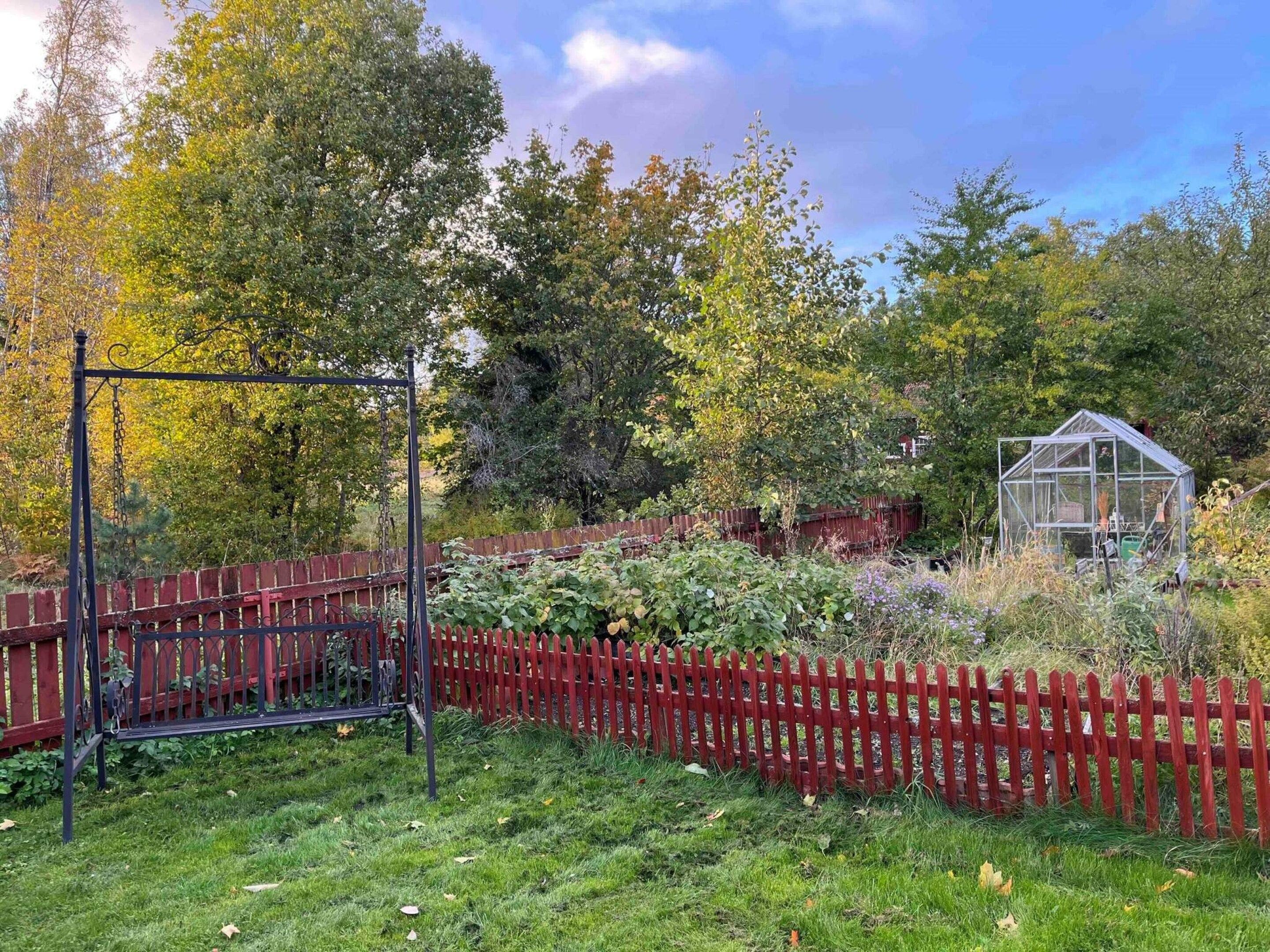 A garden with a red fence, a swing set, and a greenhouse.