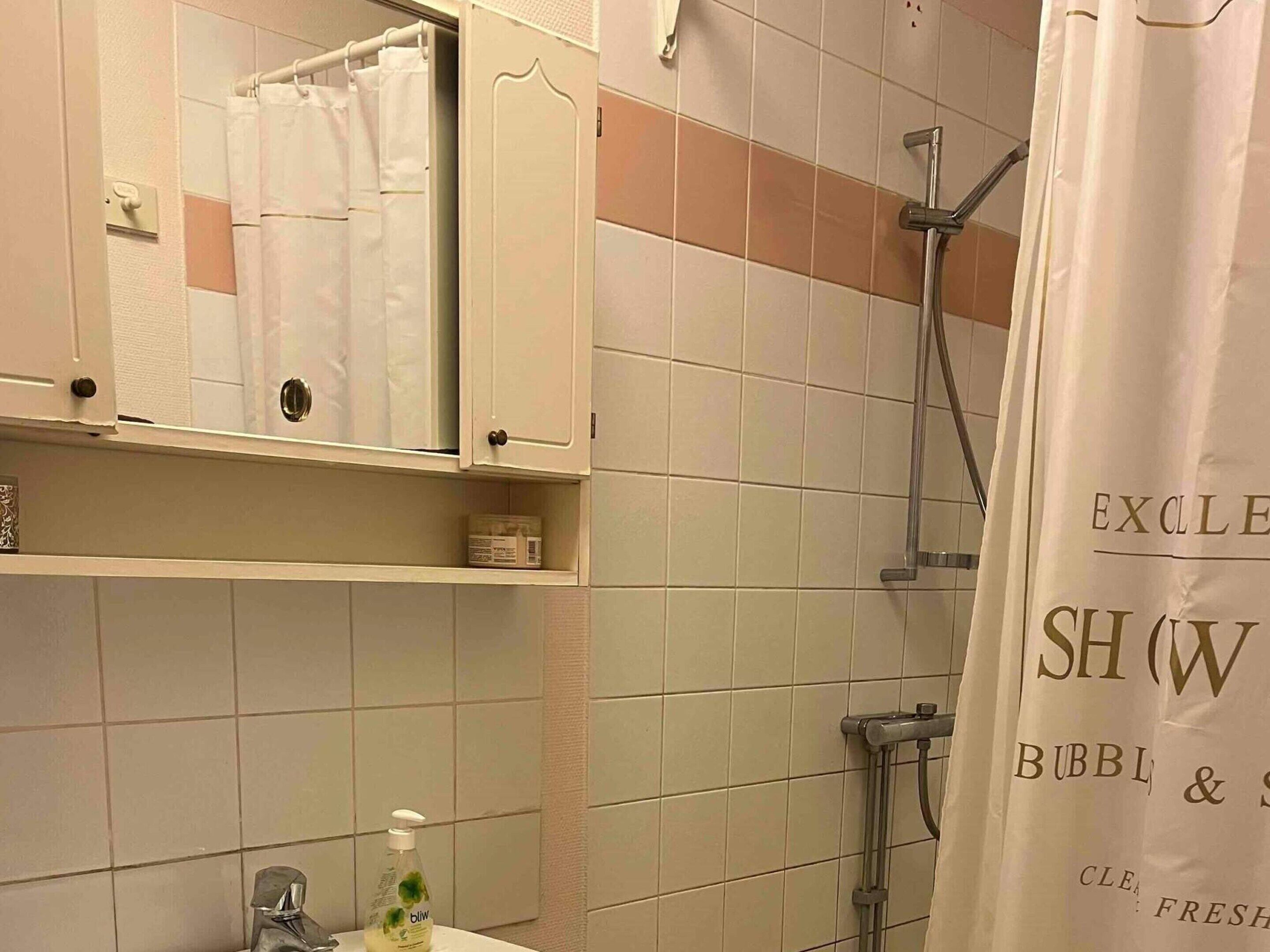 Ein Badezimmer mit Dusche, Spiegel, Waschbecken und einer Seifenspenderflasche.