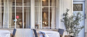 Restaurante com mesas ao ar livre, grandes janelas e um vaso de planta.