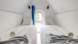 Un dormitorio con dos camas, ropa de cama blanca, una cortina azul y vistas al exterior con vegetación.