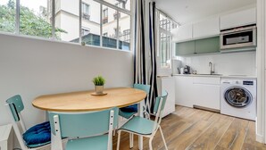 Una cocina compacta con una mesa de madera, sillas color esmeralda, lavadora y horno empotrado.