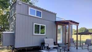 Une petite cabane à deux étages dotée d’un patio couvert comprenant un espace salon extérieur et un barbecue.