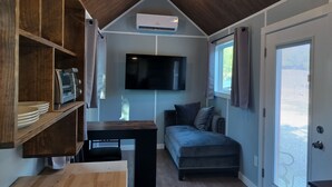 Un espace de vie compact doté d’un climatiseur intégré, d’un téléviseur à écran plat, d’un canapé et d’une table en bois.