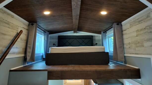 Une chambre aménagée en mezzanine avec un plafond en bois, un lit et une fenêtre.