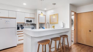 Una cocina moderna con armarios blancos, una isla central con taburetes, microondas e iluminación colgante.