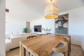 Spiseområde med et træbord, stole, en hængende lampe, et billede og en sofa i baggrunden.
