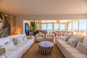 A modern living room with a large sofa, two armchairs, a round wooden coffee table, and a view of the ocean through large windows. - Luxury villa with exceptional panoramic views in Porto Vecchio (Porto-Vecchio)