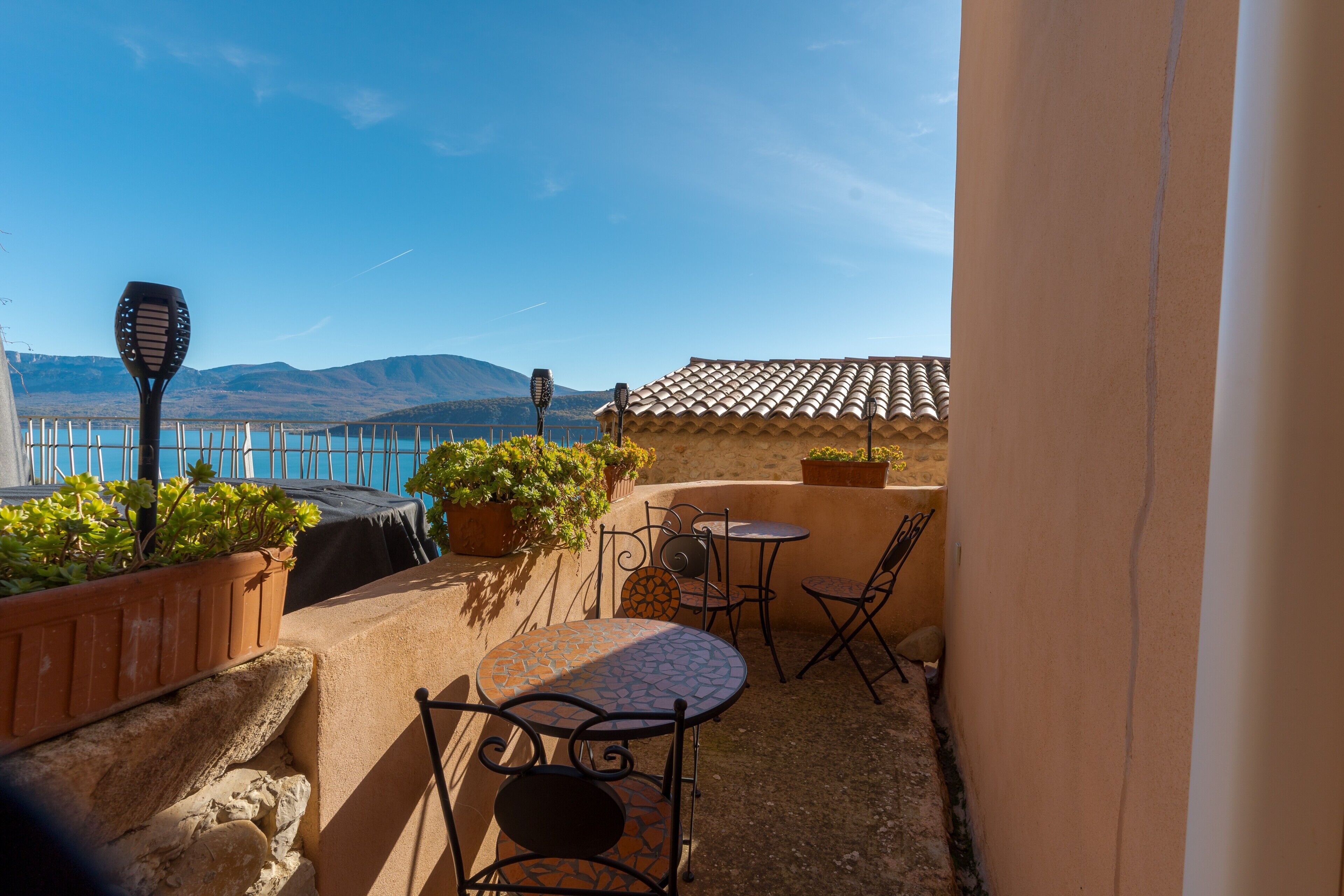 Une terrasse avec une table et des chaises, des plantes en pot et une vue sur la mer et les montagnes.