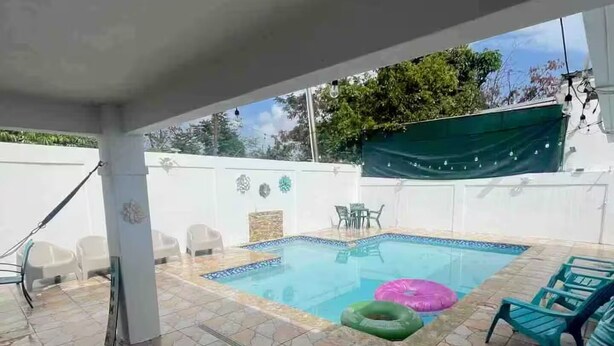 Un espace piscine doté d’un sol carrelé, d’une piscine et de plusieurs chaises longues.