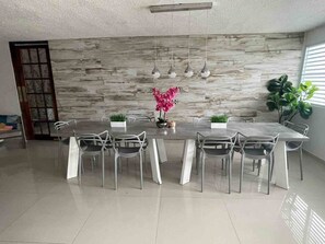 A modern dining area with a marble wall, a long table, and white chairs. - Casa Dos Palmas-House with Solar System and just 8 Min from the Airport. (San Juan)