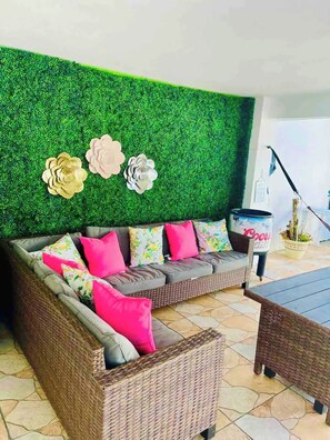 A wicker sofa with floral cushions, a green wall with decorative flowers, and a Coors Light beer can on a table. - Casa Dos Palmas-House with Solar System and just 8 Min from the Airport. (San Juan)