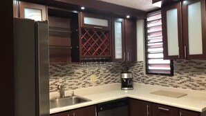 Une cuisine moderne avec des meubles de rangement en bois foncé, un réfrigérateur en acier inoxydable, une machine à café et un pare-feu en carreaux.