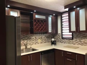 A modern kitchen with dark wooden cabinets, a stainless steel refrigerator, a coffee maker, and a tiled backsplash. - Casa Dos Palmas-House with Solar System and just 8 Min from the Airport. (San Juan)