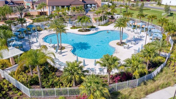 Ein Swimmingpool, umgeben von Palmen und Liegestühlen, mit Blick auf Wohnhäuser im Hintergrund.