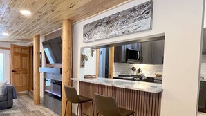 A modern kitchen with a wooden bar area, two bar stools, a microwave, and a stove.