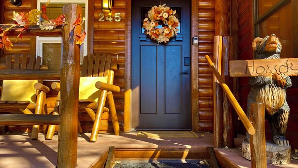 A wooden cabin with a blue door, a number '245' above it, and a wreath on the door. There are wooden chairs and a bench outside.