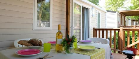 A dining table set outdoors with plates, cutlery, and a bottle of wine, surrounded by a wooden deck and a covered area.