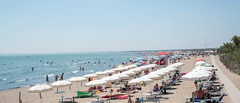 Une plage bordée de rangées de parasols et de chaises longues, un rivage sablonneux et la mer.