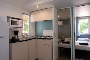 Eine kompakte Küche mit Mikrowelle, Herd und Spüle. Im angrenzenden Raum ist ein kleines Bett zu sehen.