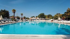 A rectangular swimming pool with clear blue water, surrounded by white lounge chairs and umbrellas. - Butterfly Vacation Park: Happy Superior Mobile Home for 7 People (Peschiera del Garda)