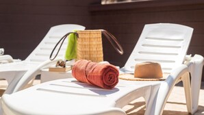 A beachside lounge area with white lounge chairs, a rolled-up towel, a straw hat, and a woven bag. - Modern apartment with private pool and beautiful views (Mogán)