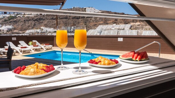 A poolside breakfast setup with croissants, strawberries, watermelon, and orange juice glasses. - Modern apartment with private pool and beautiful views (Mogán)