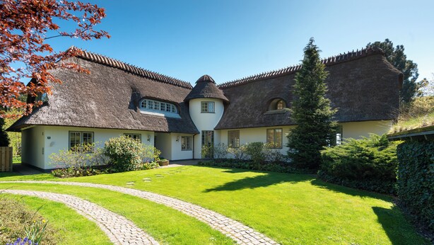 Une maison traditionnelle avec un toit de chaume, une pelouse bien entretenue et un chemin pavé de pierres.